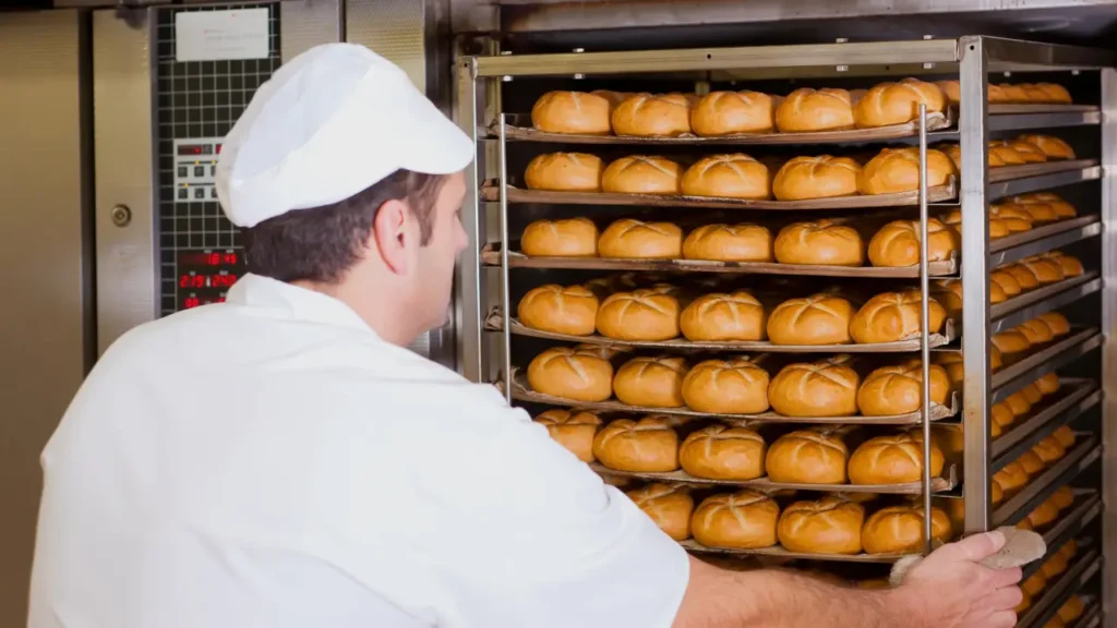 Homem mexendo em forno a gás de padaria, representando a economia local.